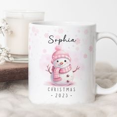 a mug with a snowman on it next to a candle