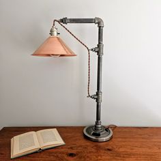 an open book sitting on top of a wooden table next to a light fixture and lamp