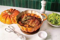 an orange casserole dish with meat and vegetables on the counter next to it