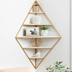 a white and gold shelf with some pictures on it next to a potted plant