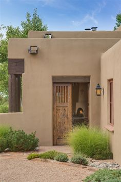 an adobe - style house with a wood door and window on the outside, surrounded by greenery