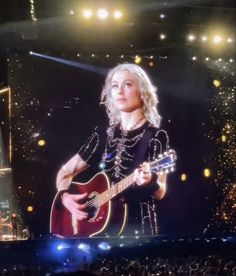 a woman holding a guitar in front of a large screen with lights and confetti on it