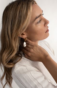 a woman with long hair wearing earrings and a white shirt is looking off to the side