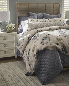 a bed with floral comforter and pillows on top of it in a bedroom next to a night stand