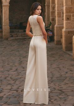 a woman standing in front of an archway wearing a white dress with beading on the back