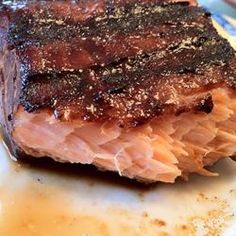 a piece of meat sitting on top of a white plate next to some sauce and seasoning