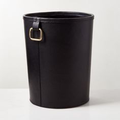 a black leather bucket with a gold buckle on the front and side, sitting on a white surface