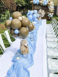 a teddy bear sitting on top of a table with blue and gold balloons attached to it