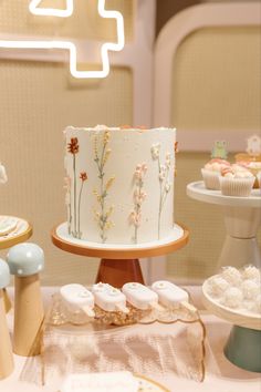 there is a white cake with flowers on it and cupcakes next to it