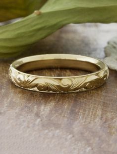 a gold wedding ring sitting on top of a wooden table next to a green plant