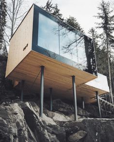 a wooden structure sitting on top of a rocky hillside next to trees and rocks with a glass window above it