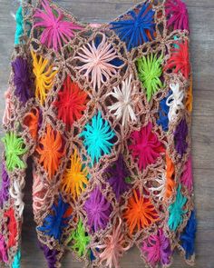 a crocheted top with multicolored flowers is hanging on a wooden surface