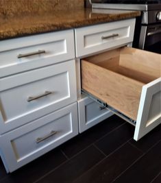 an open drawer in the middle of a kitchen counter with white cabinets and wood flooring