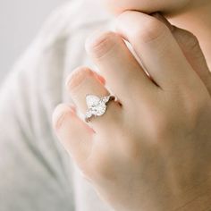 a woman's hand wearing a silver ring with a heart shaped diamond on it