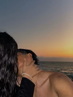 a man and woman kissing in front of the ocean at sunset or sunrise with their faces close to each other