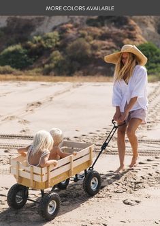 two women pushing a wooden wagon on the beach with one woman in white shirt and hat