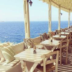 tables and chairs are lined up on an outdoor patio overlooking the ocean with umbrellas