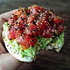 someone is holding up a sandwich with tomatoes and avocado on it, topped with sesame seeds