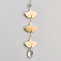 a gold and white necklace hanging from a chain on a gray wall with a glass bead in the middle