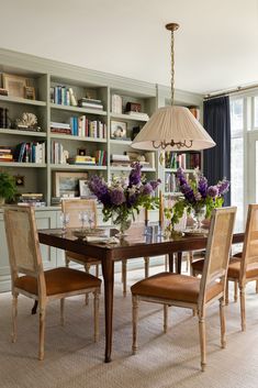 a dining room table with chairs and flowers in vases on the centerpiece, along with bookshelves