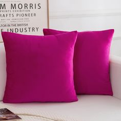 two bright pink pillows sitting on top of a white couch next to a framed photograph