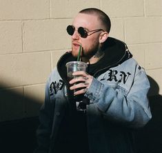 a man with sunglasses on his head drinking from a tall drink in front of a brick wall