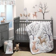 a baby crib bedding set with deer and trees on the wall next to it