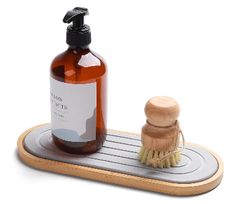 a soap dispenser and brush sit on a wooden tray with a white background