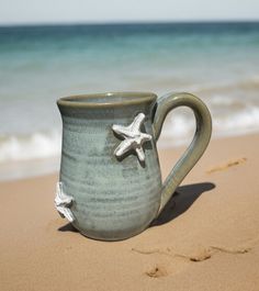 a ceramic mug sitting on top of a sandy beach next to the ocean with starfish