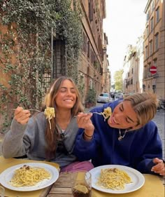 two women sitting at an outdoor table eating pasta