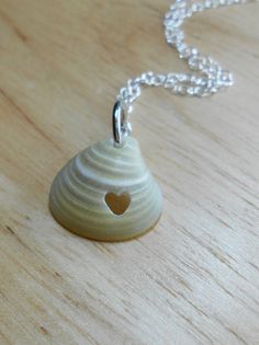 a small white vase with a heart in the center on a wooden table next to a chain