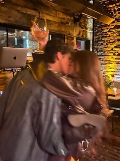 a man and woman kissing in front of a laptop computer on a wooden floor next to a brick wall