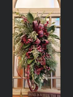 a christmas wreath with red flowers and greenery in front of an arched window that reads home is where the heart is