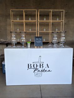 a white counter topped with glasses next to a shelf filled with bottles and wine glasses