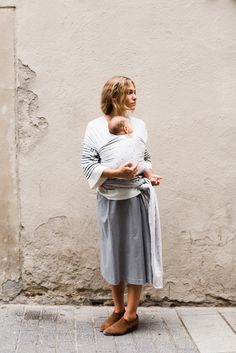 a woman holding a baby in her arms while standing on the sidewalk next to a building