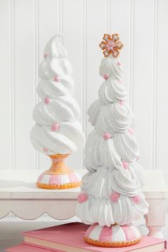 two white and pink christmas trees sitting on top of books