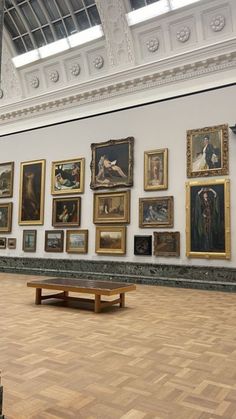 an art gallery with paintings on the wall and wooden benches in front of them,