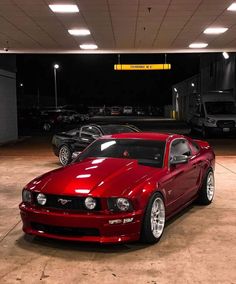 a red mustang parked in a garage next to other cars