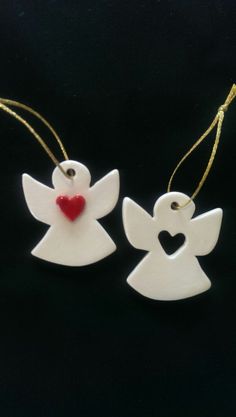 two white ceramic angel ornaments with a red heart on the end of each ornament