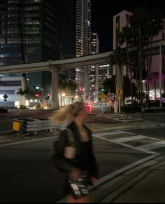 a woman walking across a street at night with buildings in the backgrouund