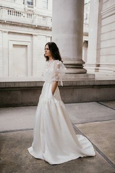 a woman in a white dress is standing on the sidewalk near some pillars and columns