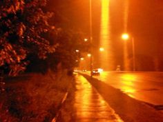 an empty street at night with lights shining on the road and trees in the foreground