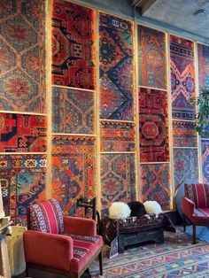 a room filled with lots of colorful rugs on the wall next to red chairs