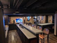 a room with a pool table, bar stools and a television in the background