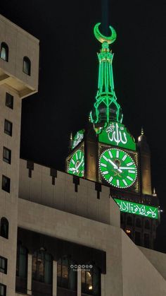 a clock tower lit up in the night with green lights on it's sides