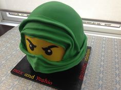 there is a cake made to look like a lego head with a green scarf on it