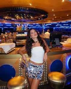 a woman standing in front of a bar with stools and lights on the ceiling