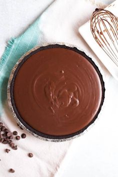 a chocolate pie sitting on top of a table next to a whisk and spoon