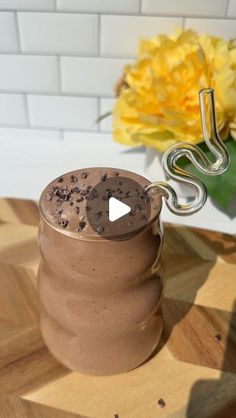 there is a chocolate drink in a glass on the table next to a yellow flower