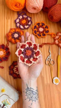 a person's hand holding a small crochet flower in front of several balls of yarn